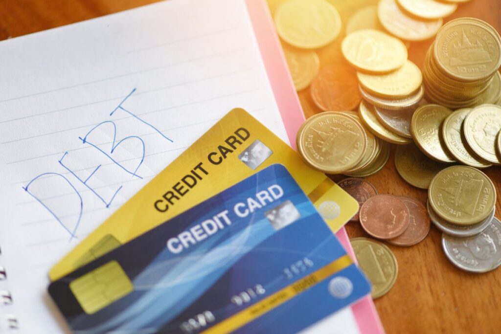 Cartões de crédito, moedas e caderno com palavra "DEBT" escrita - representando dívidas e controle financeiro