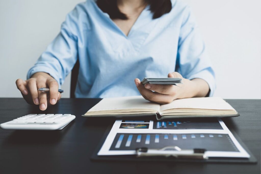 Uma pessoa sentada a uma mesa com uma calculadora, um caderno e gráficos, praticando a gestão de despesas e o controle de gastos para melhorar sua vida financeira.