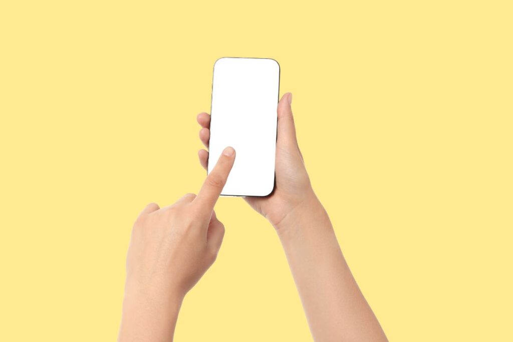 Mãos segurando e usando um smartphone com tela em branco. O ato de tocar a tela simboliza a facilidade da gestão financeira pessoal digital.