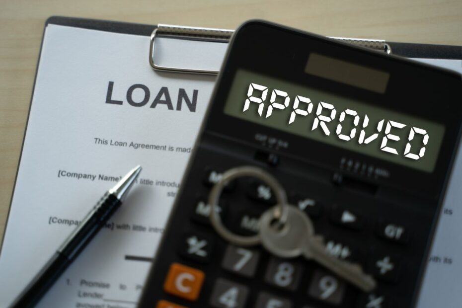 Calculadora mostrando a palavra "APROVADO" em letras brancas, ao lado de um contrato de empréstimo. Simboliza a aprovação de um pedido de crédito pessoal.