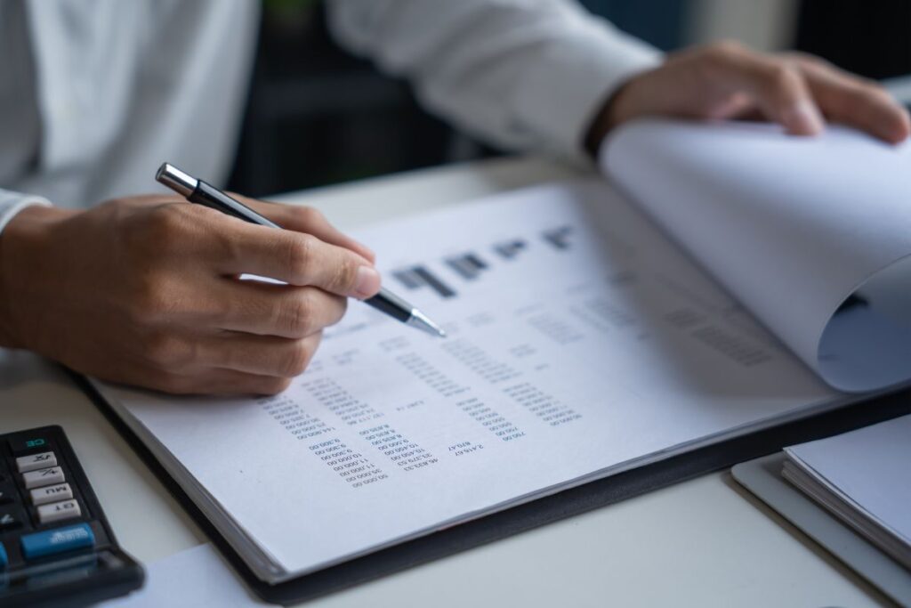 Pessoa analisando planilha financeira com caneta e calculadora desenvolvendo mentalidade financeira através do controle de gastos