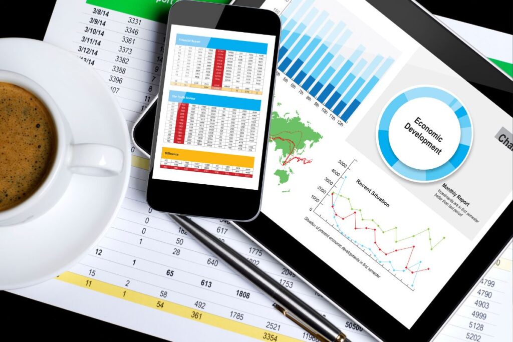 Uma xícara de café, uma caneta, um tablet e um smartphone exibindo relatórios de planejamento financeiro, destacando a utilização da tecnologia na análise de dados.