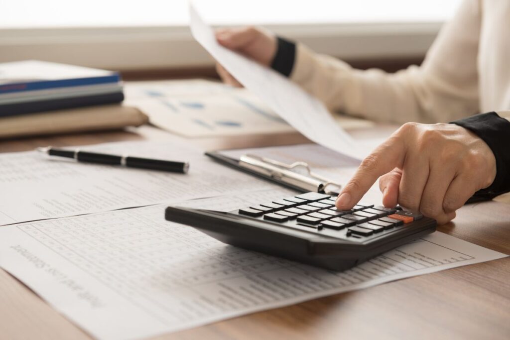 Uma pessoa usando uma calculadora para gerenciar contas e documentos de planejamento financeiro, focando no cálculo de orçamentos.