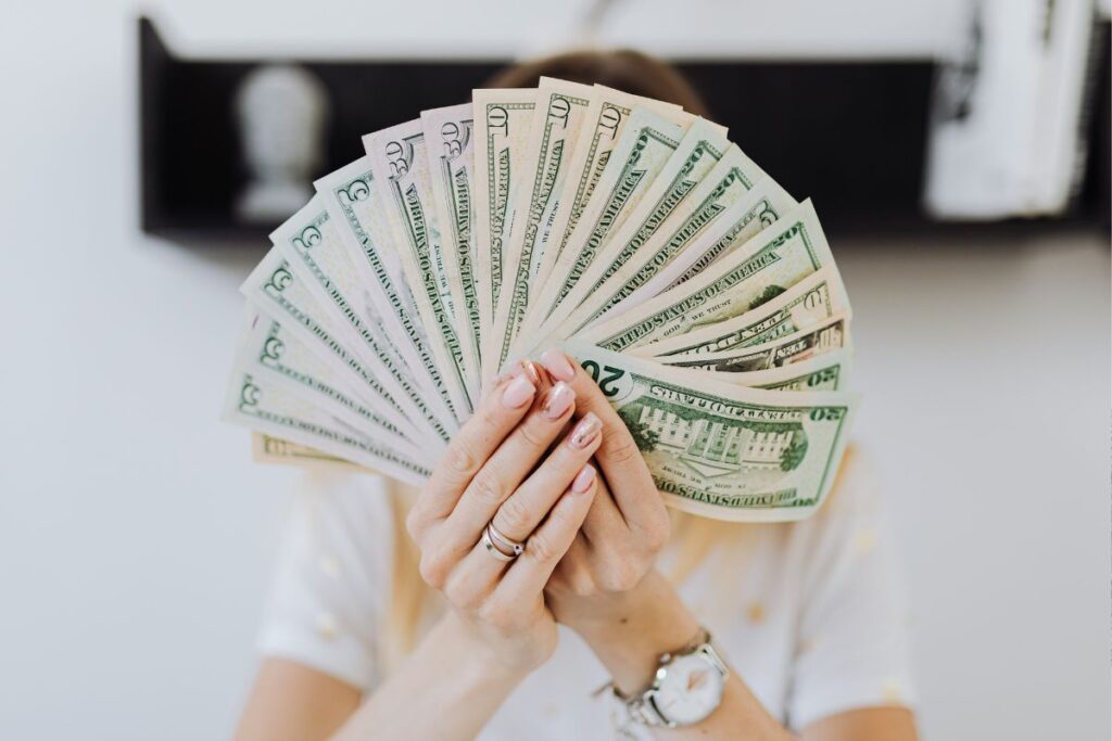 Mulher segurando leque de cédulas de dólar representando sucesso na geração de renda extra