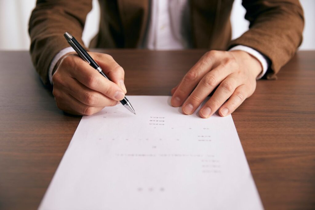 Pessoa assinando contrato de seguro com caneta sobre mesa representando formalização de apólice