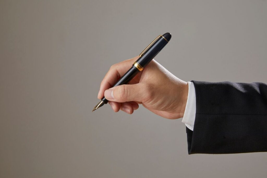 Mão executiva segurando caneta tinteiro representando assinatura de apólice de seguro e termos contratuais