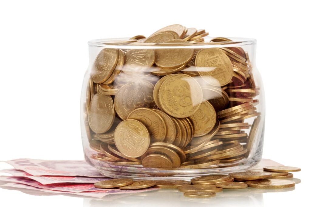 Pote de vidro cheio de moedas e notas representando reserva de emergência completa e controle financeiro eficiente
