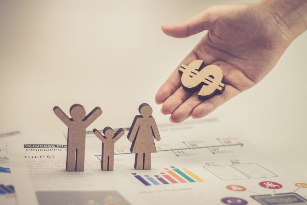 Mão segurando símbolo de dólar sobre figuras de família em planejamento financeiro para reserva de emergência familiar