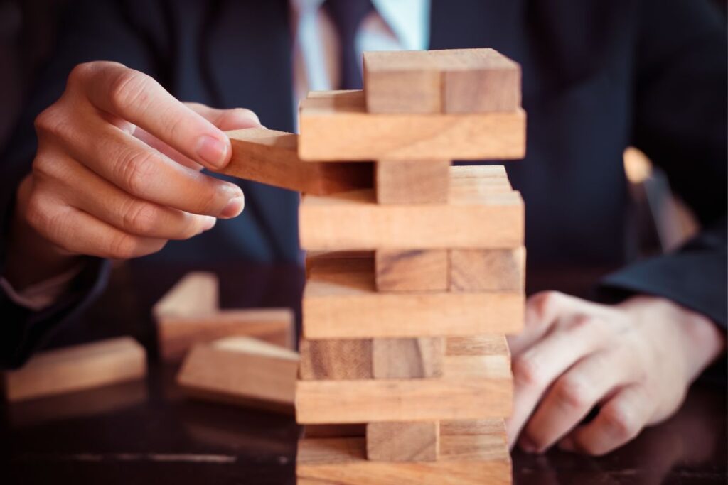 Mão de executivo removendo um bloco de uma torre, representando a gestão de riscos e oportunidades e a estratégia de um empreendimento.