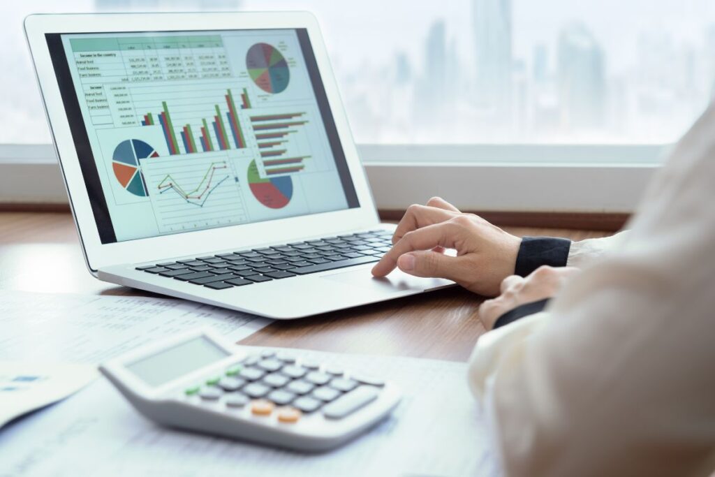 Pessoa analisando gráficos financeiros em laptop com calculadora e documentos representando planejamento e educação financeira prática