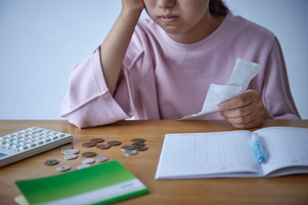 Mulher preocupada analisando contas e despesas com moedas e calculadora sobre mesa representando desafios da educação financeira pessoal